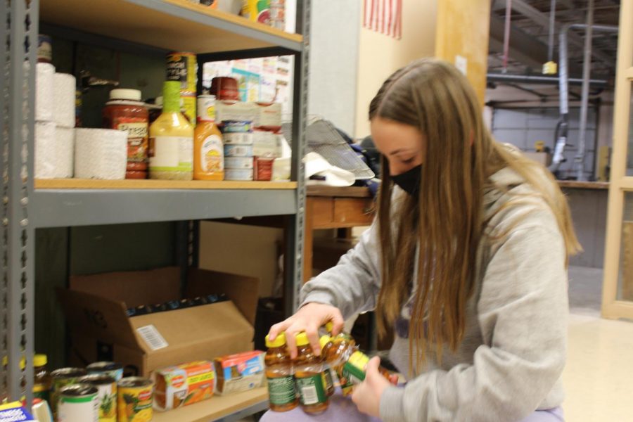 Hayley Hines, freshman, puts apple juice on the food pantry shelves on Mar. 4. Hines loves the food pantry because it helps people in need. Its a good thing we have this food pantry because a lot of families need it, Hines said.